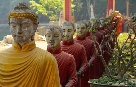 Several Buddhist statues in a row, the first one in yellow and red in the Following in Hpa-An, Myanmarの写真素材
