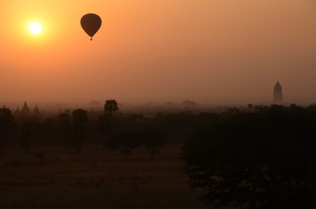 A hot-air balloon is flying in an orange, yellow sky, some temples are visible in the background, longshotの写真素材