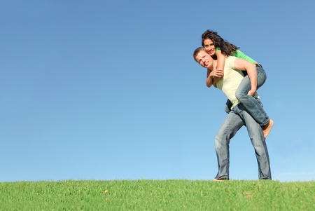 happy smiling couple outside on grass giving piggy back in summerの写真素材