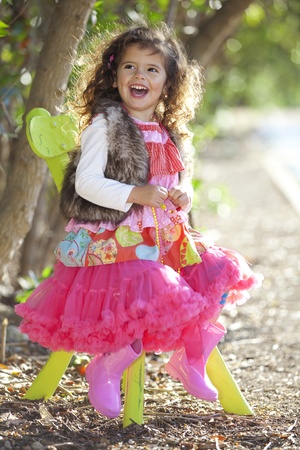 happy smiling little girl in colourful clothes sitting outdoors in chairの写真素材