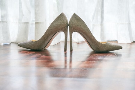 The women's shoes glittering on the wooden floor, the sun light behind the white curtain, the shadow of the shoes on the floor - low angleの写真素材