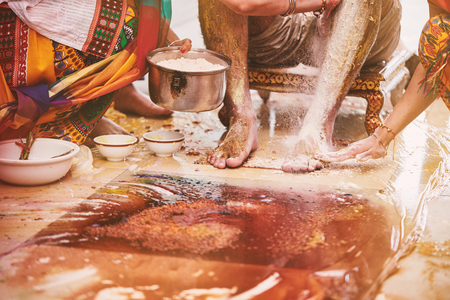 The groom sitting while the family and relatives members pasting turmeric powder (haldi) oil mixed with milk before bathing (snan), traditional rituals for Indian marriageの写真素材