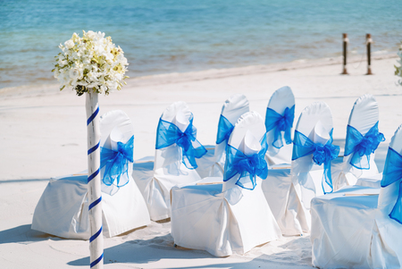 The random white spandex chairs cover with blue organza sash decoration waiting for beach wedding venue setupの写真素材