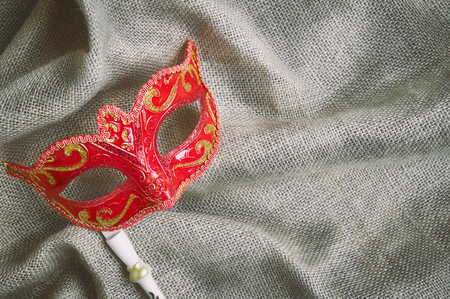 Closeup red carnival mask, Venetian mask (Opera mask) with white wood handle on the burlap sackcloth Fantasy concept, Photo booth propsの写真素材