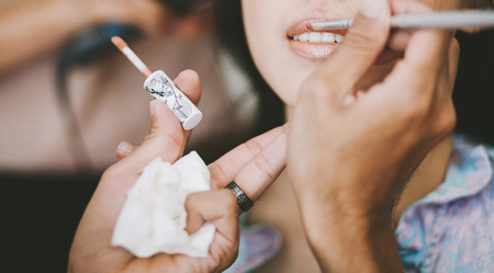 Makeup artist applying lipstick for a young Asian woman during getting ready for wedding ceremonyの写真素材