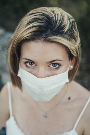 Blonde masked girl in nature landscape during the pandemic.の写真素材