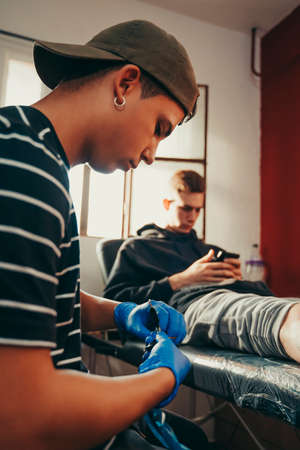 Young tattoo artist picking up roll of paper in a tattoo studio.の写真素材