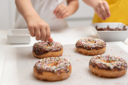 Children decorating donuts with colorful splashes in the kitchen at homeの写真素材