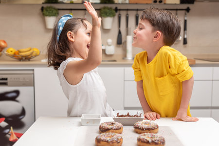 Happy children after decorating chocolate donuts with colorful sprinkles in the kitchen at home
