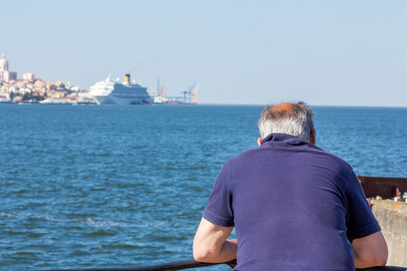 An old person looking at a passenger ship docked at Tagus river, Lisbon, Portugalの写真素材