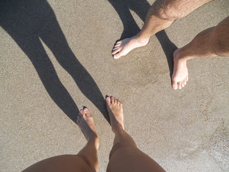Low section view of a man and women  young couple legs  standing on sand on the beach  at noon...