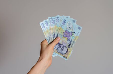 Close up view of a woman's hand holding a pile of Romanian lei  money on a gray background . The economic impact of coronavirus  in  est Europe countries .の写真素材