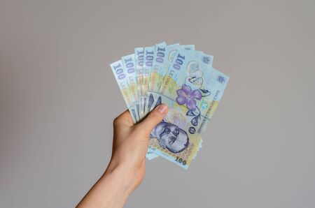 Close up view of a woman's hand holding a pile of Romanian lei  money on a gray background . The economic impact of coronavirus  in  est Europe countries .