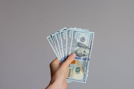 Close up view of a woman's hand holding a pile of 100 dollar banknotes   money on a gray background...
