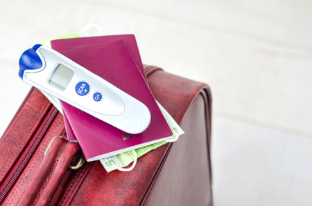 Close-up of  digital thermometer, passports and face mask on a suitcase for travel or business...