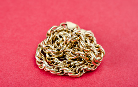 Close-up of   yellow  neck  gold chain on a red background representing the concept of wealth or...