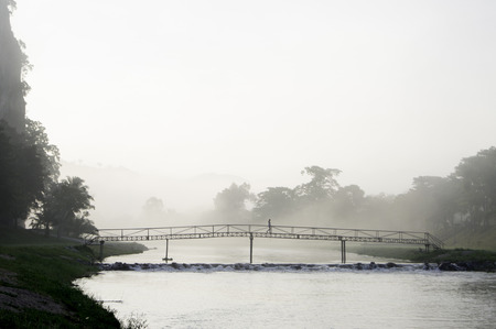 lonely lady crossing a bridge in the misty morningの写真素材