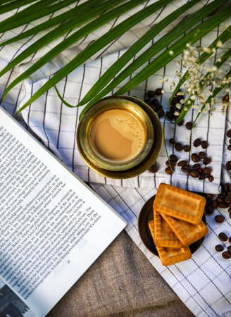 top view of indian morning drink the masala tea with some glucose biscuits on the side and a book