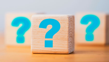 Three wooden blocks are arranged in a row, each displaying a large, bright blue question mark. The background is blurred.の写真素材