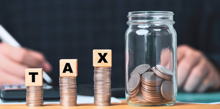 Coins stacked to spell TAX, with a jar full of coins, suggesting financial planning and saving for tax season.の写真素材