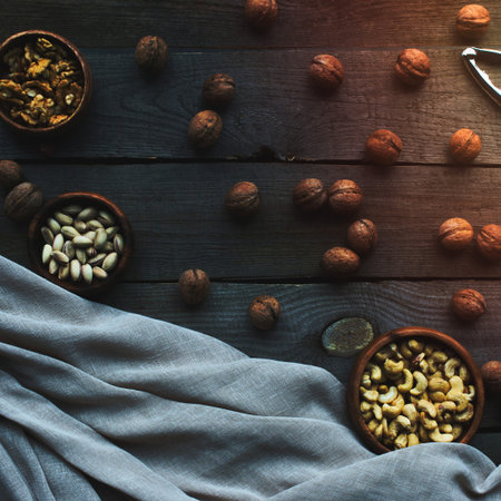 A top-down view of various nuts and dried fruits scattered across a dark wooden surface, with a blue cloth draped on one side.の写真素材