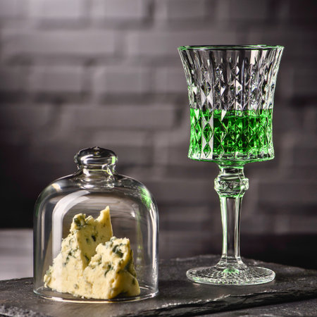 A vibrant green beverage in an ornate glass sits beside a glass cloche covering a small appetizer or food item.の写真素材