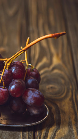 A close-up shot of deep red grapes with a thin stem, resting on a weathered wooden background.の写真素材