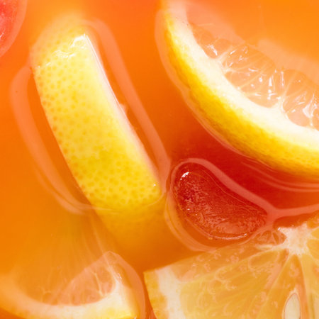 Close-up view of bright orange liquid with vibrant yellow lemon slices and hints of red, suggesting a refreshing drink.の写真素材