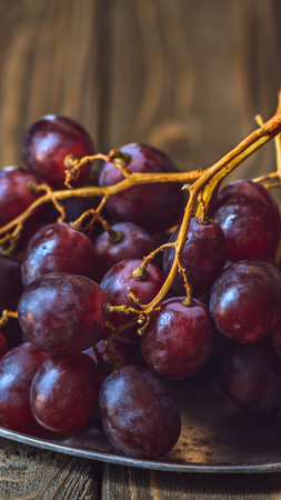 A detailed view of deep red grapes with a natural sheen, resting on a textured wooden background, highlighting their fresh appearance.の写真素材