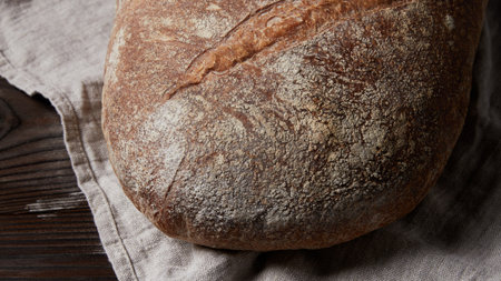 A close-up view of a freshly baked, crusty artisan bread loaf dusted with flour, resting on a textured linen cloth.の写真素材
