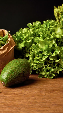 A ripe avocado and a bunch of vibrant green leafy vegetables are artfully arranged on a rustic wooden table.の写真素材