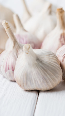A close-up shot of several whole garlic bulbs with papery skins, resting on a rustic white wooden background.の写真素材