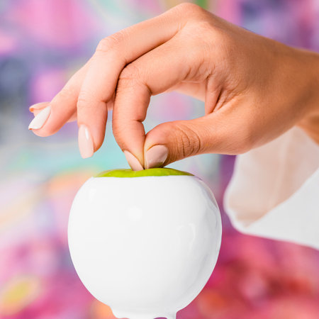 A close-up shot shows a hand delicately placing a tiny green sprout into the top of a white, apple-shaped planter.の写真素材