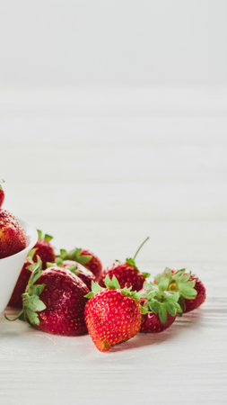 A close-up shot of vibrant red strawberries, some halved, artfully arranged on a light-colored wooden background.の写真素材