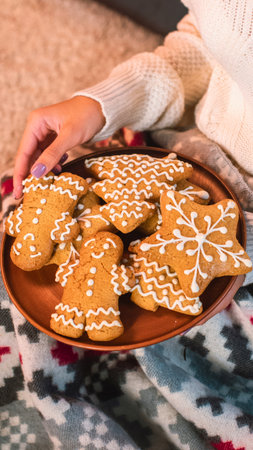 A close-up of a wooden plate filled with decorated gingerbread cookies. A hand reaches to take one.の写真素材