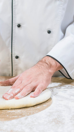 A close-up shot of a chef in a white uniform expertly kneading a ball of dough on a floured wooden surface.の写真素材