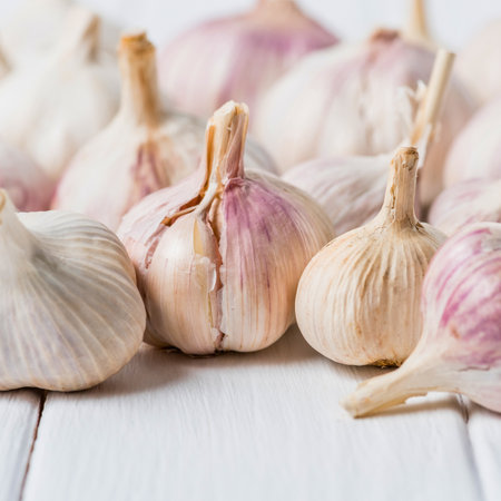 A close-up shot of several whole garlic bulbs with papery skins and visible roots, arranged on a rustic white wooden background.の写真素材