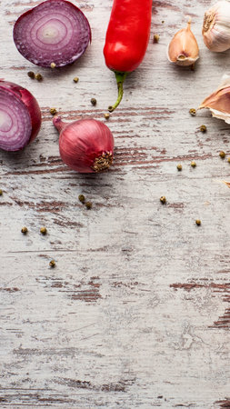 A vibrant arrangement of fresh red onion halves, a red chili pepper, garlic cloves, and scattered peppercorns on a weathered wooden surface.の写真素材