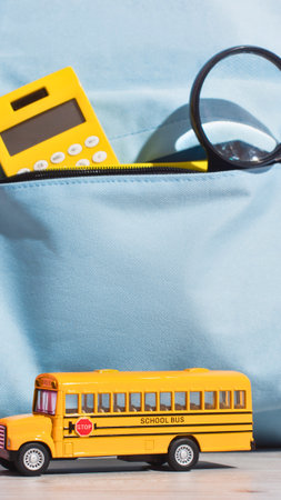 A yellow toy school bus sits below a pocket holding a calculator, pencil, and magnifying glass, hinting at learning and exploration.の写真素材