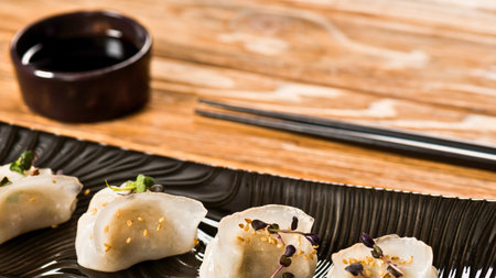 Close-up of delicate sushi pieces, a small dish of soy sauce, and chopsticks resting on a textured bamboo mat.の写真素材