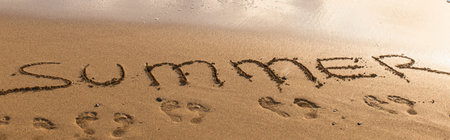 The word "SUMMER" is written in dark sand, with tiny footprints scattered below it.の写真素材