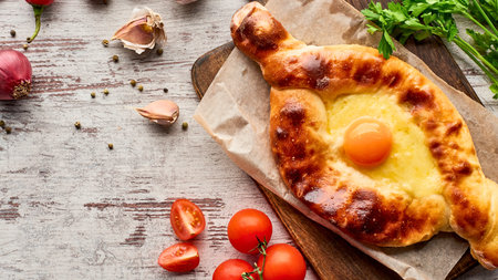 A close-up shot of a golden-brown khachapuri, a traditional Georgian cheese bread, topped with a runny egg and served with fresh vegetables.の写真素材
