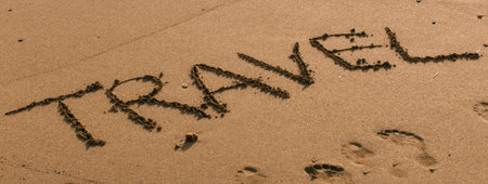 The word TRAVEL is written in dark, rough lettering on a textured, sandy background. It suggests adventure and journeys.の写真素材