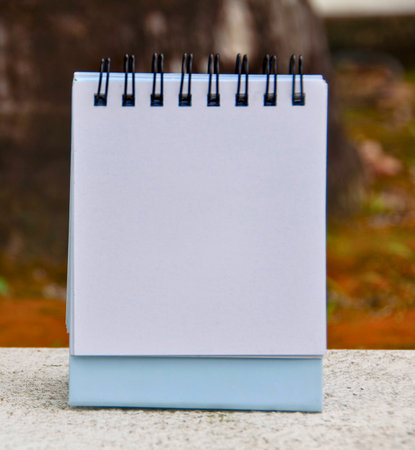 A blank spiral-bound desk calendar sits on a surface, ready for notes or planning. The background is softly blurred.の写真素材