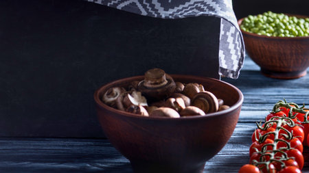 A close-up shot of earthy mushrooms in a dark bowl, with vibrant green sprouts and ripe cherry tomatoes nearby on a wooden surface.の写真素材
