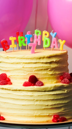 A close-up of a tall, layered cake decorated with red candies and topped with colorful BIRTHDAY...