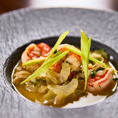 Close-up of succulent shrimp in a rich broth, topped with vibrant green herbs, served in an elegant, dark textured bowl.の写真素材