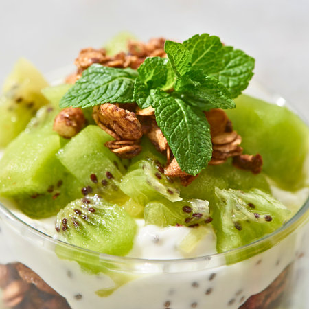 A refreshing parfait layered with creamy yogurt, diced kiwi, crunchy walnuts, and fresh mint leaves.の写真素材