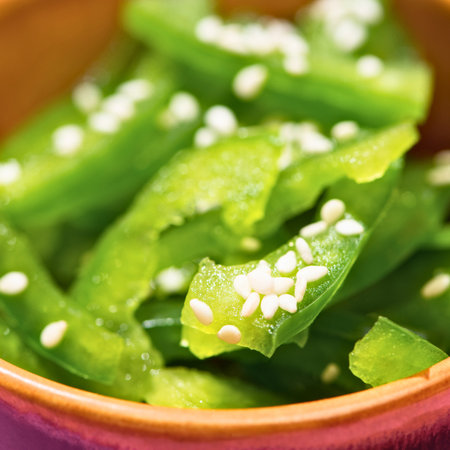 A vibrant, close-up shot of thinly sliced green bell peppers, sprinkled with white sesame seeds, in a rustic bowl.の写真素材