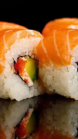Fresh salmon sushi rolls filled with creamy avocado and bright orange roe, presented on a reflective surface.の写真素材